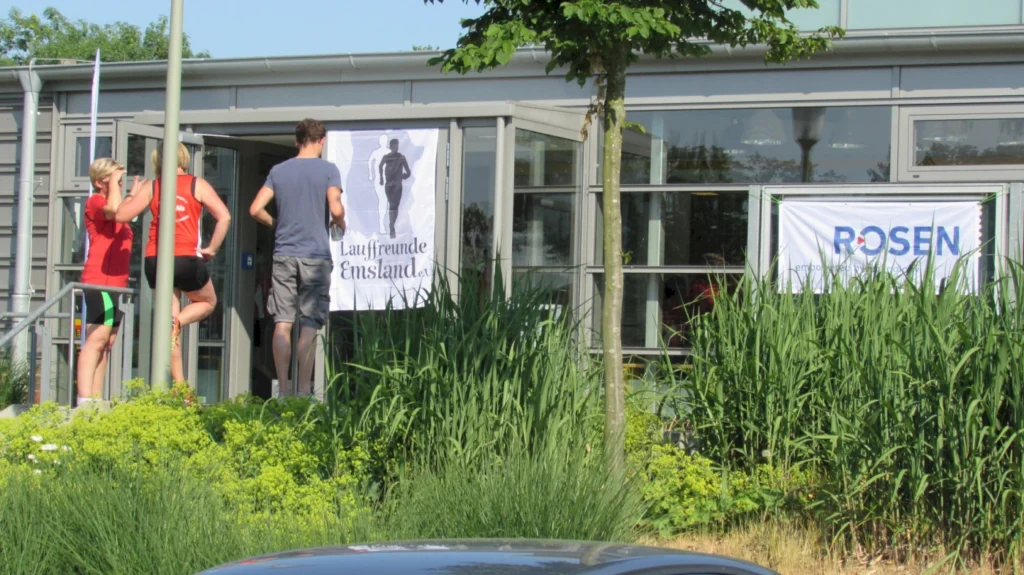 Personen betreten ein Gebäude mit Bannern von Lauffreunde Emsland und Rosen bei einer Laufveranstaltung.