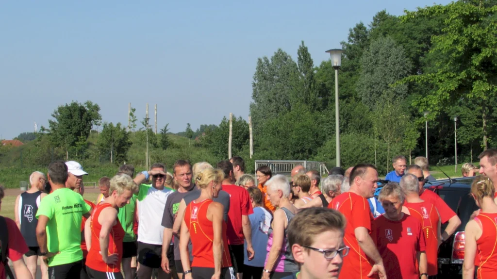 Läufergruppe in bunter Sportkleidung versammelt sich draußen vor einem Lauf, umgeben von grüner Landschaft und Bäumen.