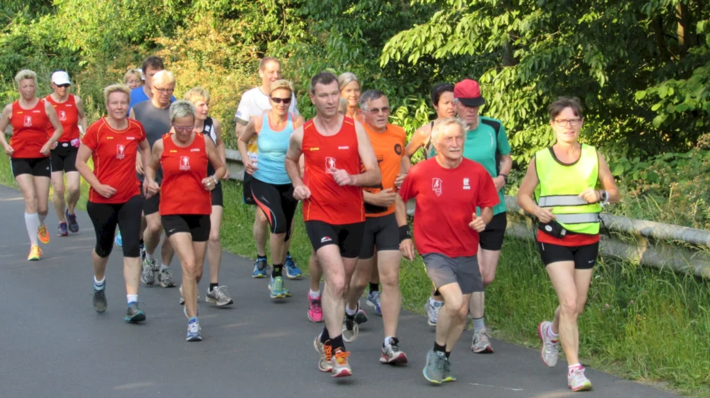 Gruppe von Personen beim Joggen im Freien, alle in sportlicher Kleidung, auf einer von Bäumen gesäumten Straße.