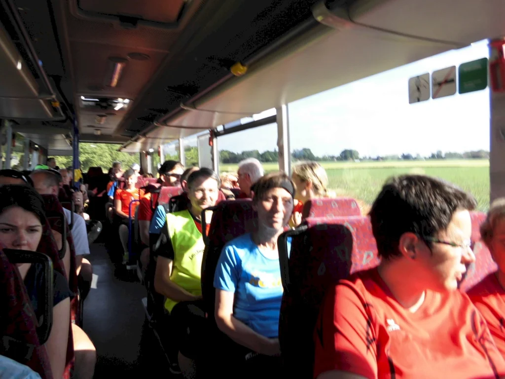 Mehrere Personen sitzen in einem fahrenden Bus, Tageslicht strömt durch die Fenster.