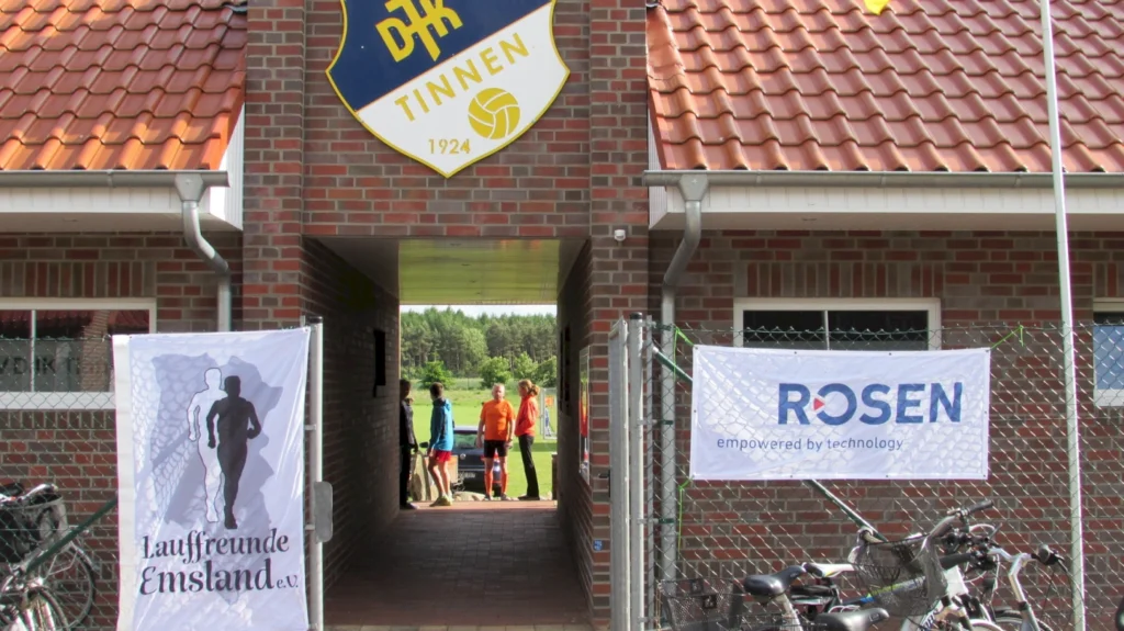 Eingang des DJK Tinnen Vereinsheims mit Bannern der Lauffreunde Emsland und Rosen Group, Fahrräder im Vordergrund.