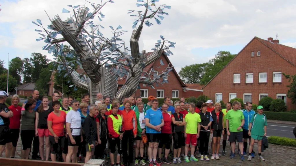 Gruppe von Menschen in Sportkleidung posiert vor Metallskulptur eines Baumes in einer urbanen Umgebung.