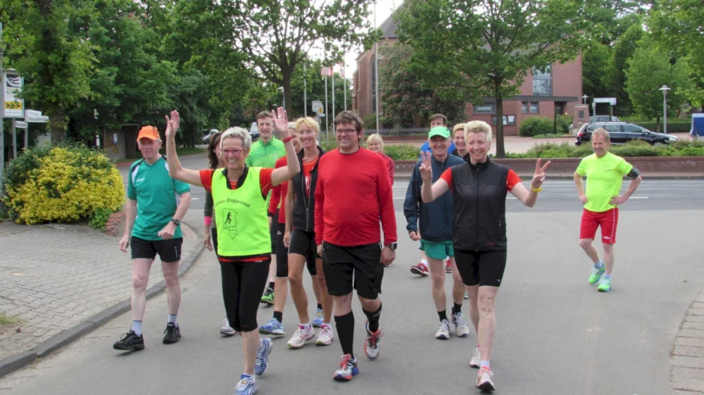 Läufergruppe beim Stadtlauf in bunter Sportkleidung, fröhlich und motiviert auf einer Straße bei Sonnenschein.