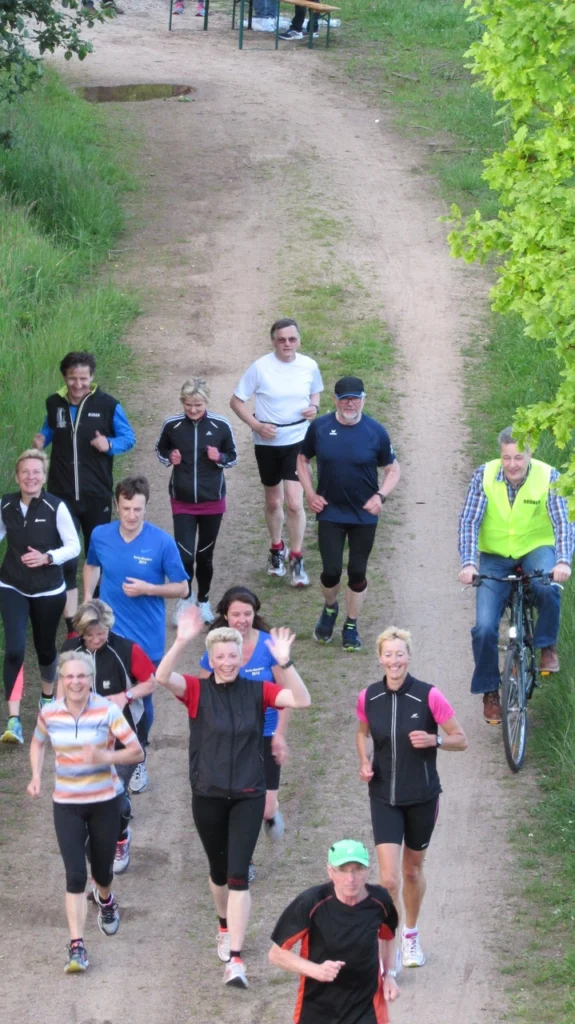 Gruppe von Läufern auf einem Waldweg bei einem sportlichen Event, begleitet von einem Radfahrer.