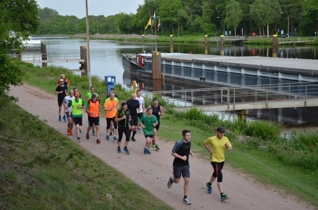 Läufergruppe joggt entlang eines Kanals in grüner Umgebung bei einem Freizeitevent.