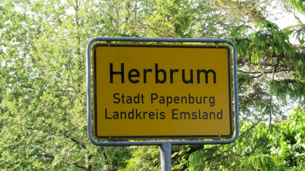 Ortsschild von Herbrum, Stadt Papenburg im Landkreis Emsland, umgeben von grüner Natur.