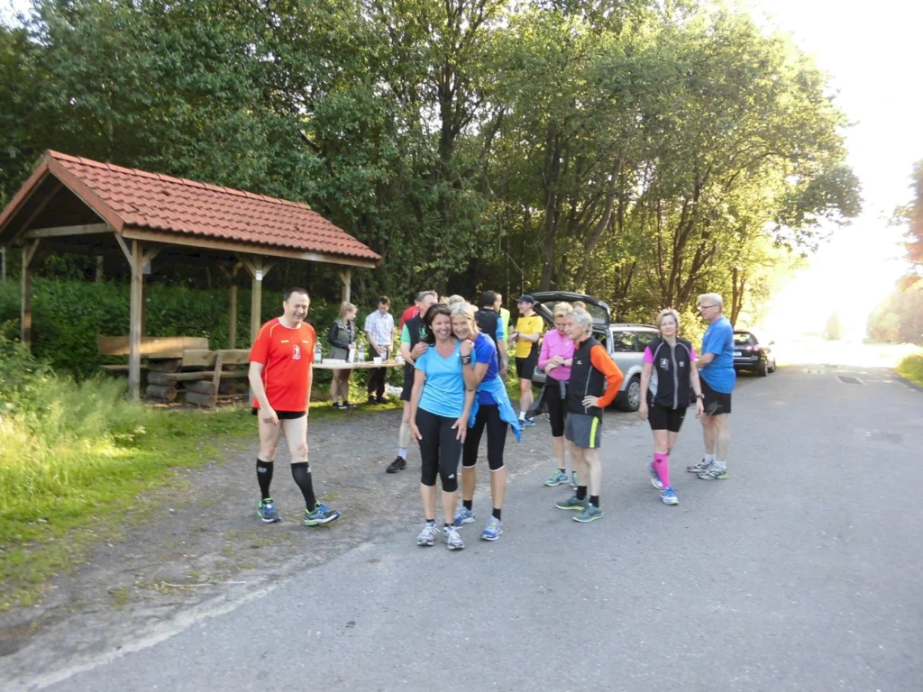 Gruppe von Läufern in Sportkleidung versammelt sich an einem sonnigen Tag neben einem Pavillon im Grünen.