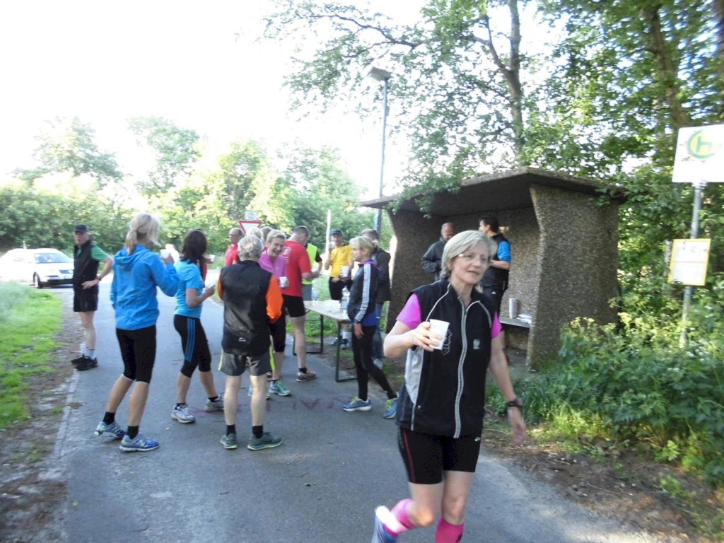 Läufergruppe bei Raststation im Grünen, trinken Wasser während eines sommerlichen Marathons.