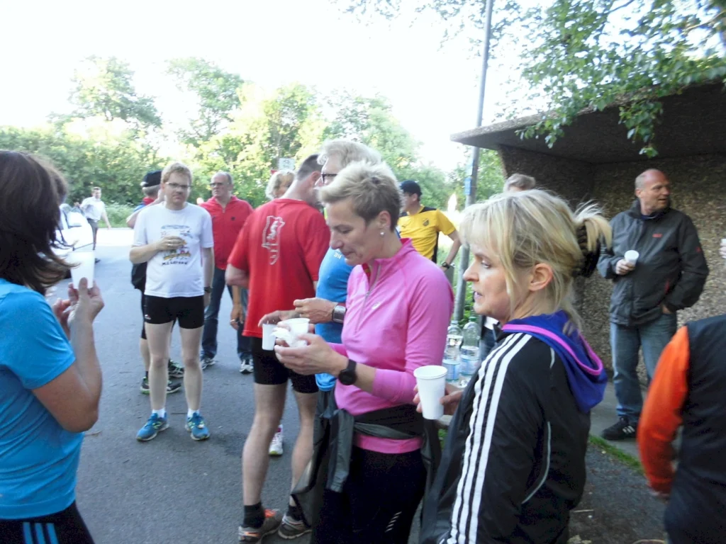 Personengruppe beim Laufen pausiert zum Trinken im Freien, umgeben von Bäumen.