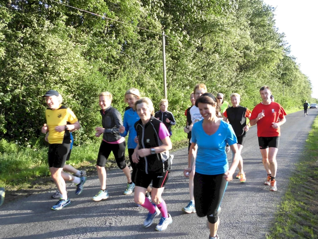 Gruppe von Joggern läuft fröhlich auf einer sonnenbeschienenen Straße im Grünen.