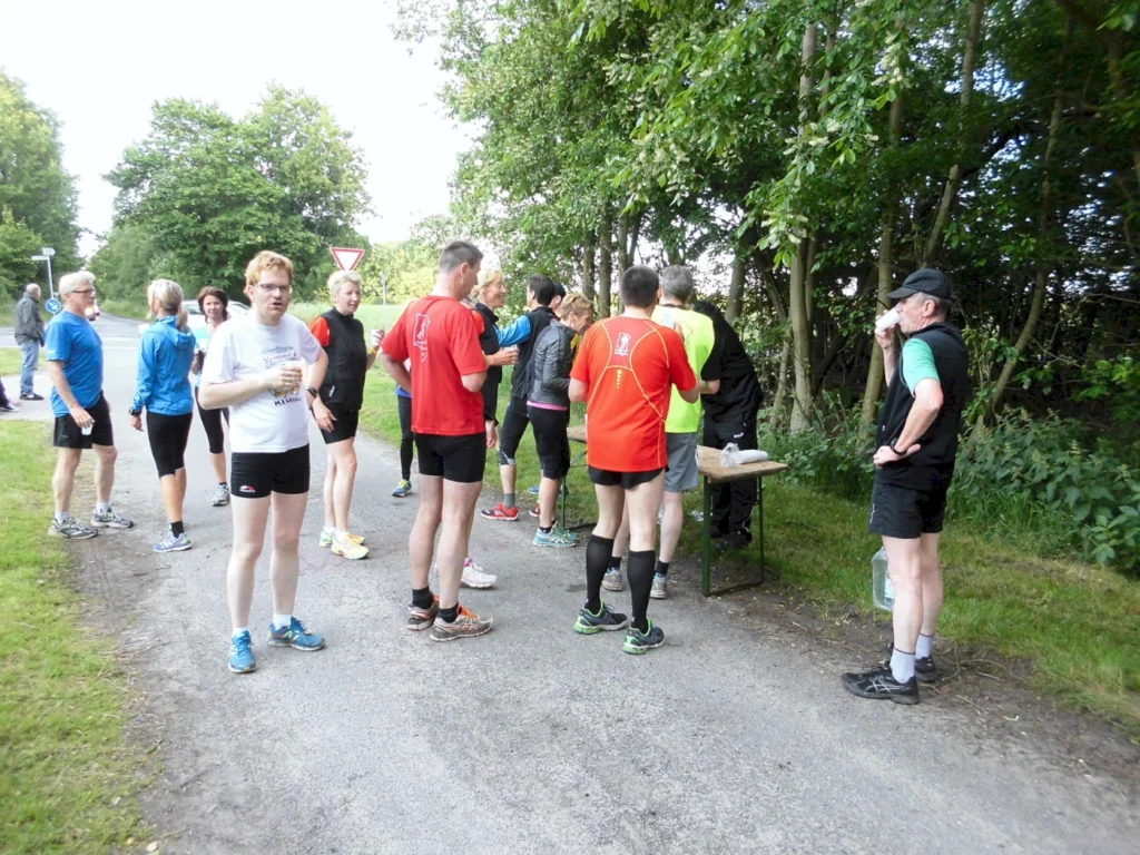 Läufergruppe erfrischt sich bei einem Wettkampf im Freien neben Bäumen, während einer Pausenstation auf einer Landstraße.