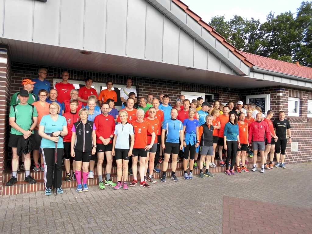 Gruppe von Läufern in bunter Sportkleidung posiert vor einem Backsteingebäude nach einem Lauftraining.