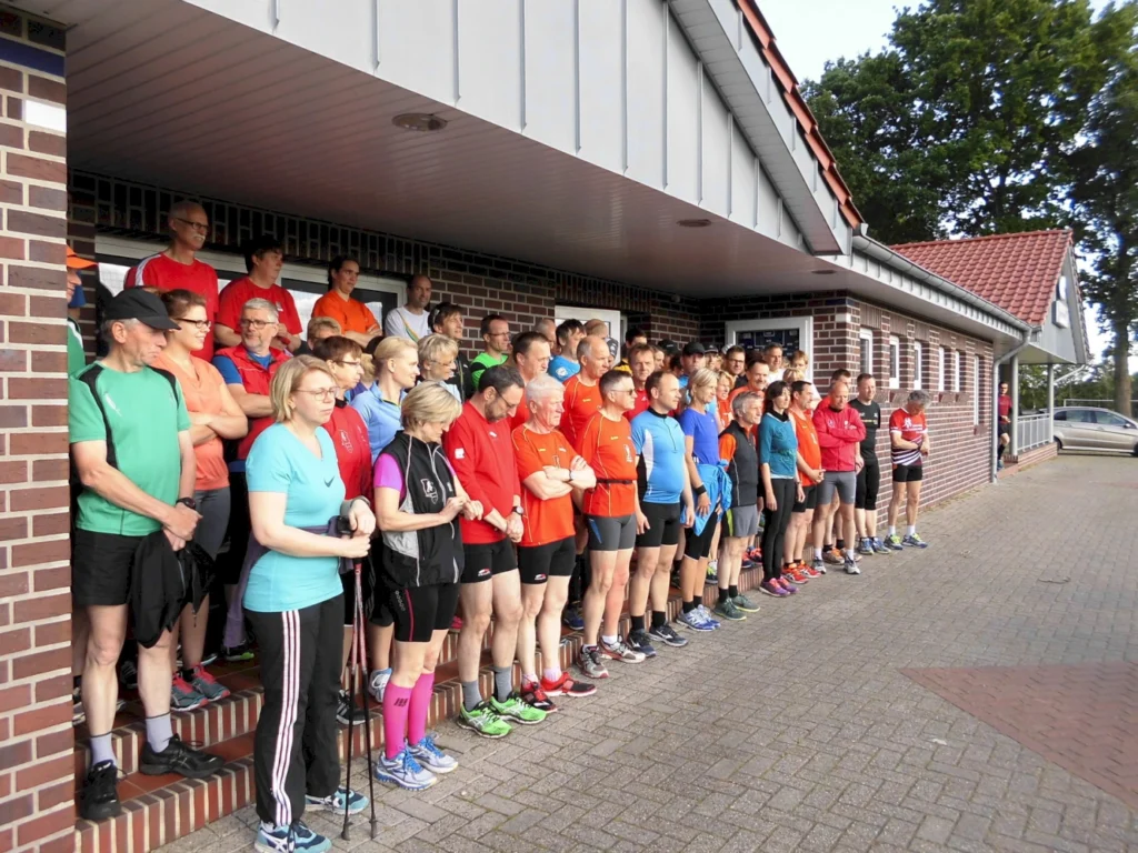 Gruppe von Läufern in sportlicher Kleidung, die vor einem Gebäude stehen. Die Teilnehmer sind in verschiedenen Farben gekleidet und warten auf den Start eines Events. Im Hintergrund ist ein modernes Gebäude und eine grüne Umgebung sichtbar.