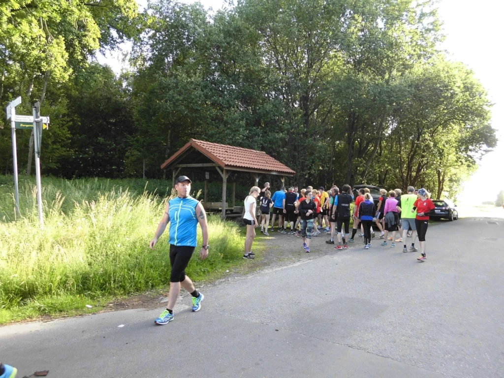 Läufergruppe beim Treffen im Park, umgeben von Bäumen, mit Sportbekleidung und fröhlicher Stimmung.