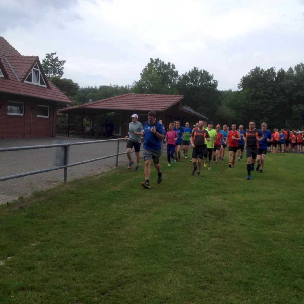 Läufergruppe joggt auf grünem Rasen neben Ziegelgebäude; Freizeitlauf, Gemeinschaftssport im Freien.