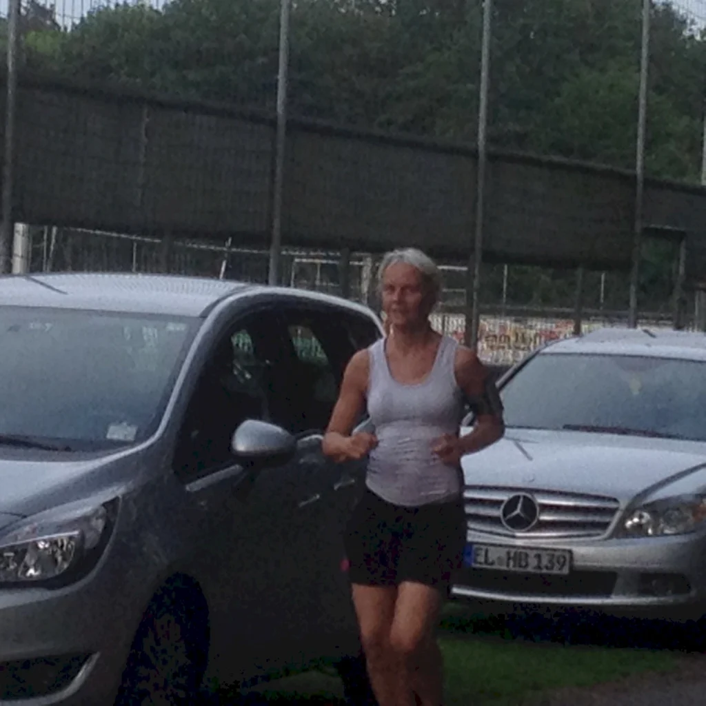 Person joggt im Freien neben geparkten Autos, trägt Sportkleidung und einen Handyhalter am Oberarm.