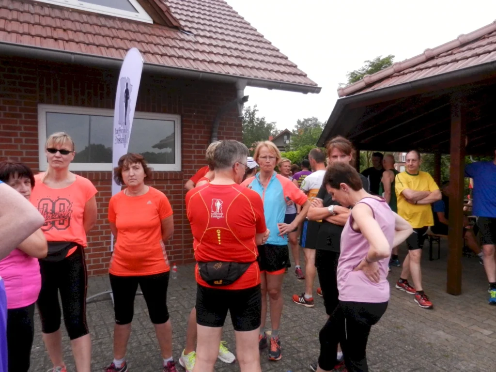Gruppe von Läufern bei einem Lauf-Event versammelt sich draußen neben Backsteingebäude und Pavillon im Gespräch.