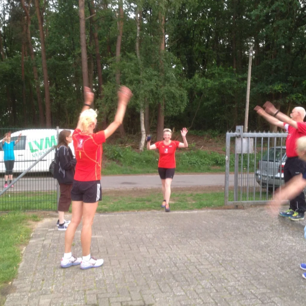 Menschen in roten Shirts machen Sportübungen im Freien vor einem Wald, Gesundheit und Fitness im Sommer.