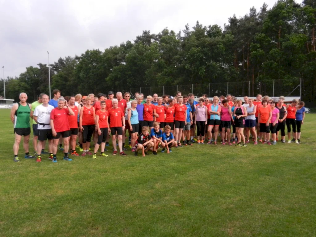 Gruppenfoto von Läufern in roten Trikots auf einem Sportplatz, umgeben von Bäumen, ideal für Sport- und Laufveranstaltungen.