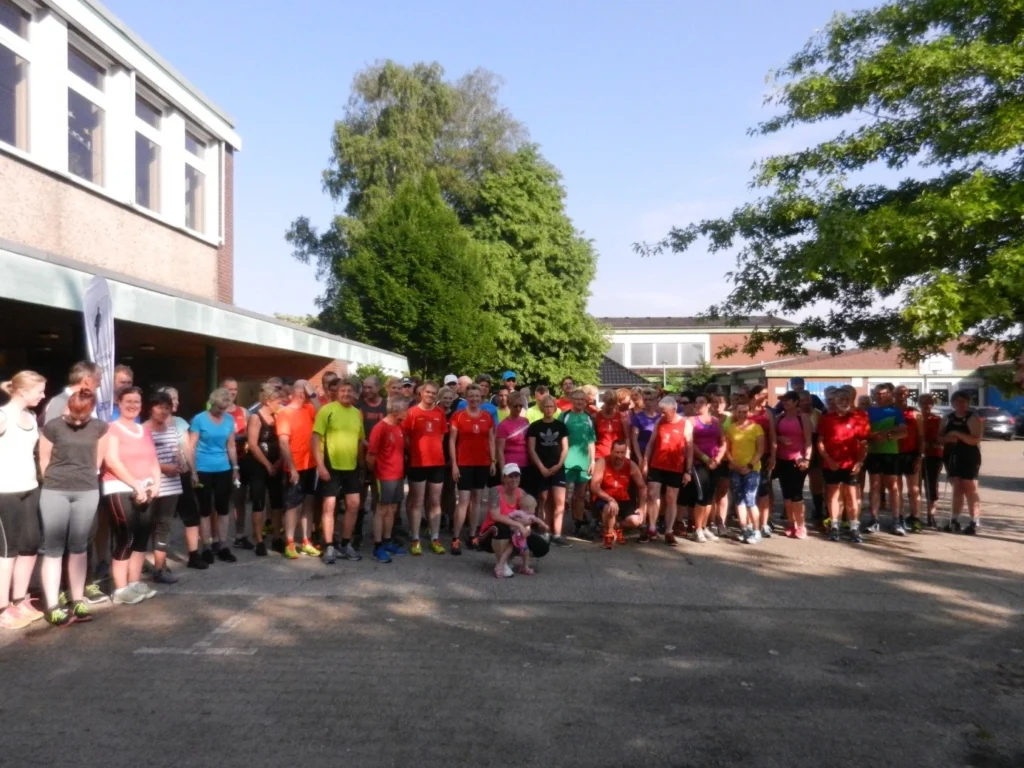 Große Laufgruppe in bunter Sportkleidung vor einem Schulgebäude, bereit für einen gemeinsamen Lauf bei sonnigem Wetter.