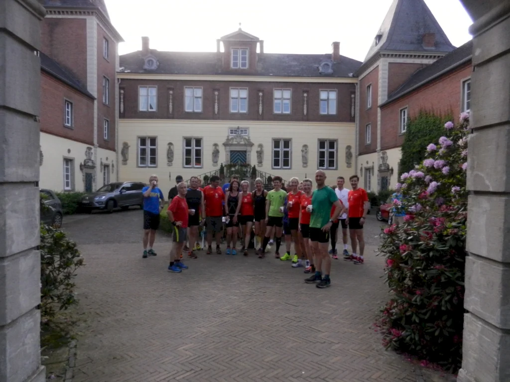 Gruppe von Läufern steht vor historischem Gebäude in Schlossinnenhof, umgeben von blühenden Rhododendren.