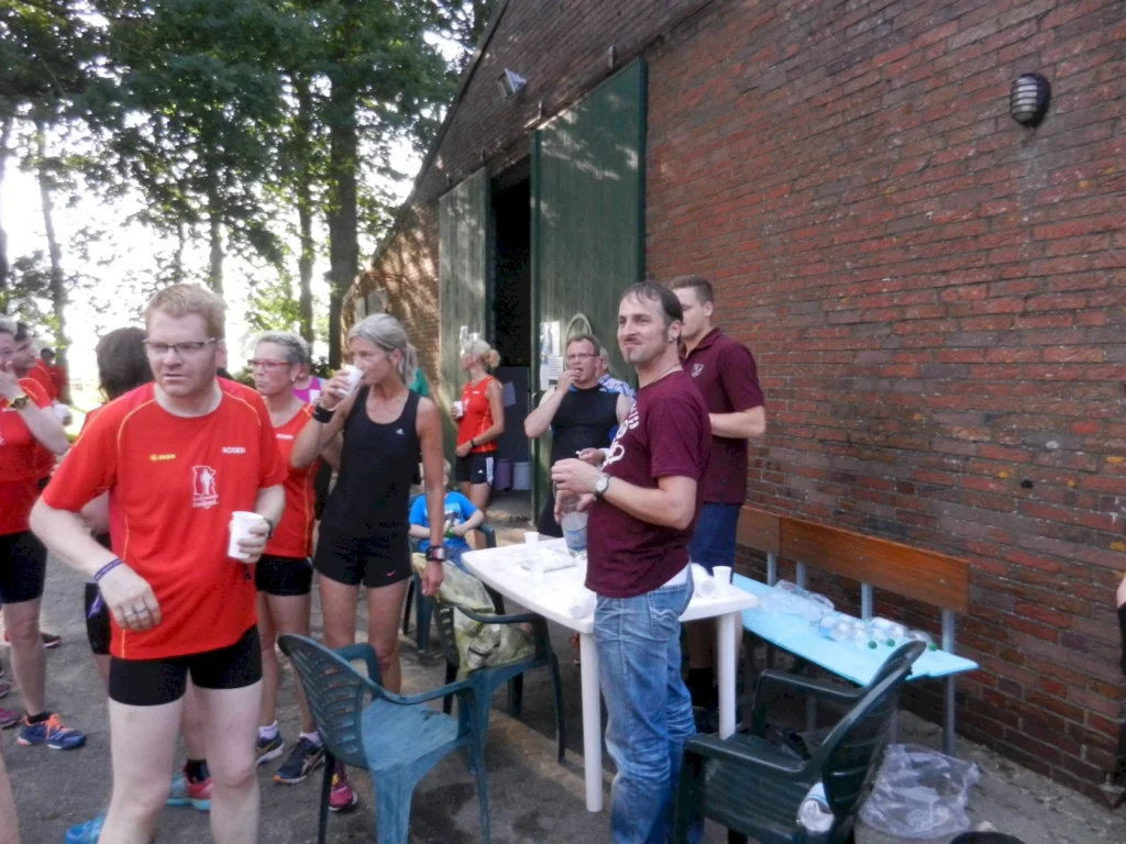 Personen bei einem Lauf-Event erholen sich mit Getränken vor einer Backsteinwand im Freien.