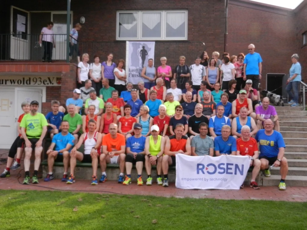 Große Gruppe von Teilnehmern eines Lauftreffs vor dem Vereinsgebäude Kurzwold 93 e.V., viele tragen bunte Sportkleidung.
