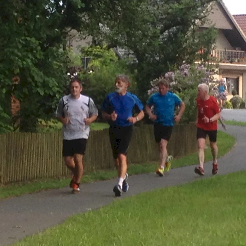 Vier Männer joggen auf einem Weg in einem grünen Park, entspannte Freizeitaktivität.