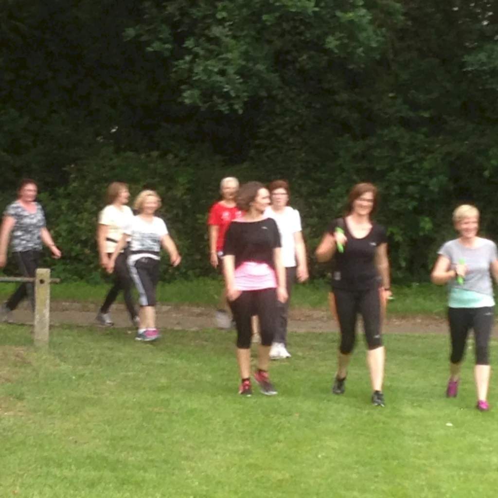 Gruppe von Frauen beim Nordic Walking im Park an einem bewölkten Tag. Fitness und Gemeinschaft im Freien.