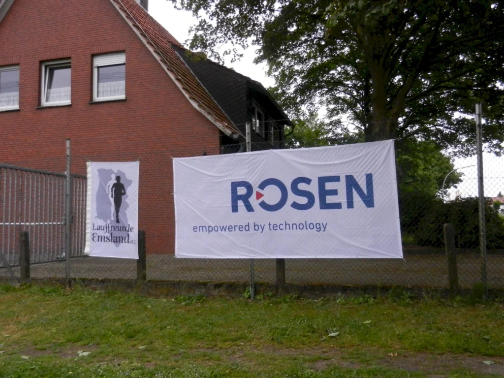 Banner von Lauffreunde Emsland und ROSEN mit Schriftzug empowered by technology vor einem Backsteinhaus.