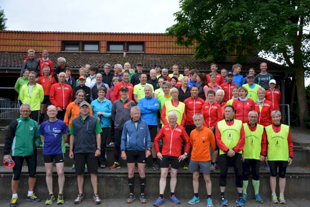 Große Gruppe von Läufern in bunter Sportkleidung posiert auf Treppenstufen vor einem Gebäude, bereit für ein Event.
