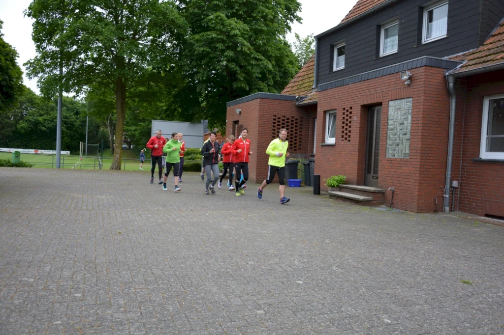 Eine Gruppe von Läufern joggt bei bewölktem Wetter in einem Wohngebiet an roten Backsteinhäusern vorbei.