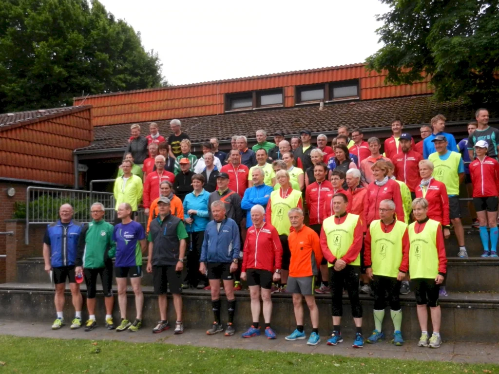 Gruppe von Läufern versammelt für ein Gruppenfoto bei einer Laufveranstaltung vor einem Backsteingebäude.