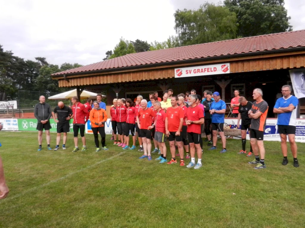 Gruppe von Leuten in Sportkleidung steht vor einem Vereinsgebäude im Freien bei SV Grafeld e.V. mit grüner Wiese.