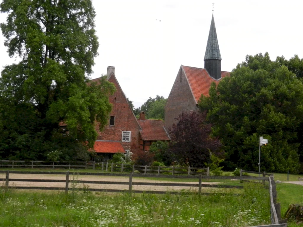 Historische Backsteinkirche mit Turm und umgebenden Bäumen hinter einem Holzzaun. Ländliche Idylle in Deutschland.