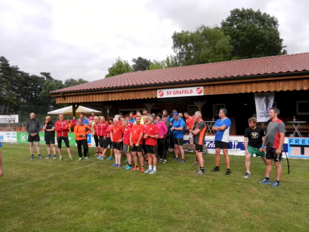 Gruppe von Menschen in Sportkleidung vor Vereinsheim „SV Graefeld“ auf Rasenfläche, bereit für sportliche Aktivitäten.