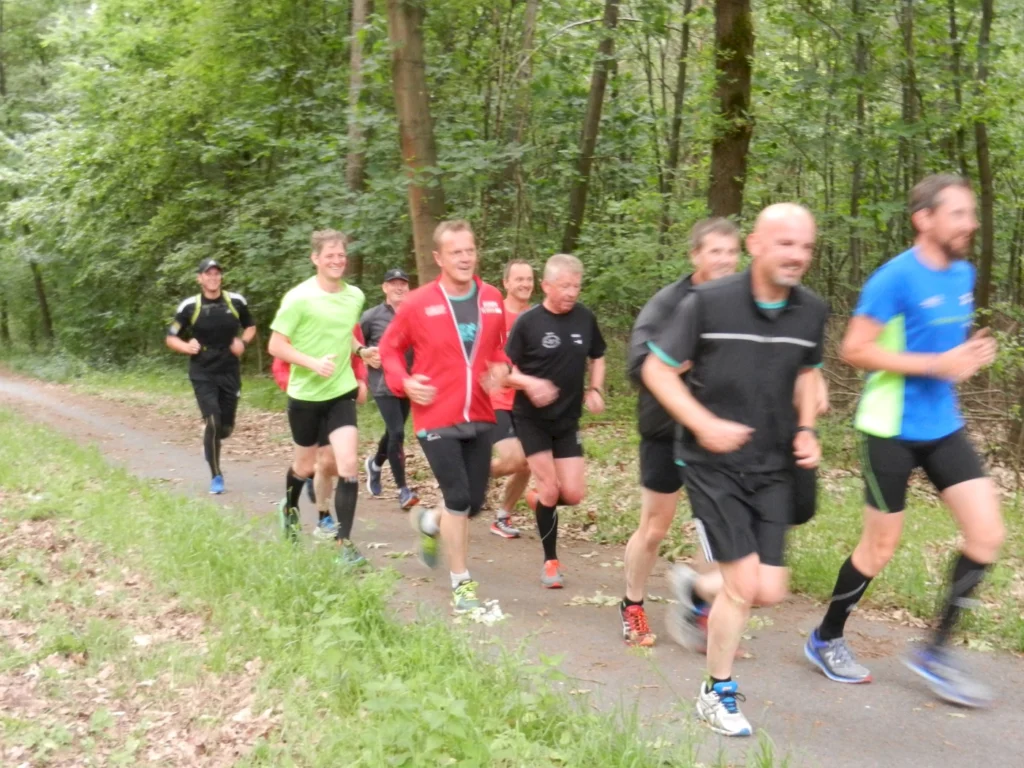 Eine Gruppe von Männern joggt auf einem Waldweg bei Tageslicht und genießt das gemeinsame Laufen in der Natur.