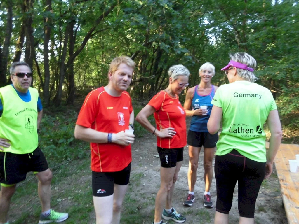 Gruppe von Menschen in Sportkleidung bei einer Pause im Wald, lächelnd und redend.