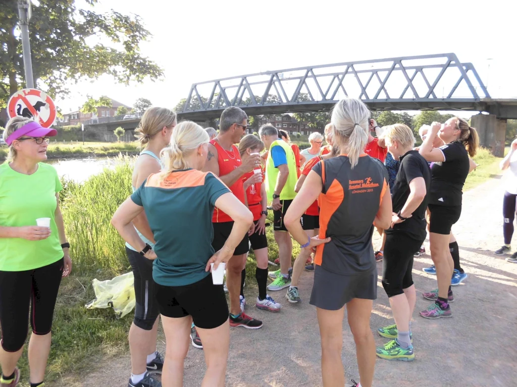 Gruppe von Läufern pausiert nach dem Training am Fluss, begleitet von einer Brücke im Hintergrund.
