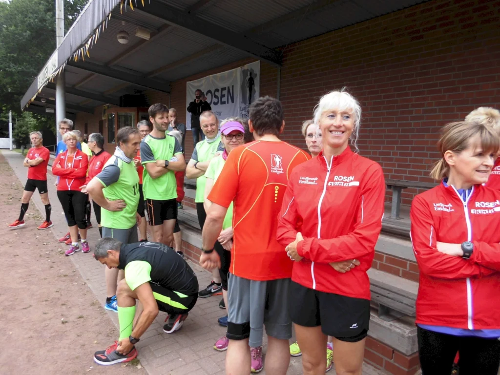Läufergruppe in roten und grünen Trikots versammelt sich vor einem Gebäude für ein Event oder Training im Freien.
