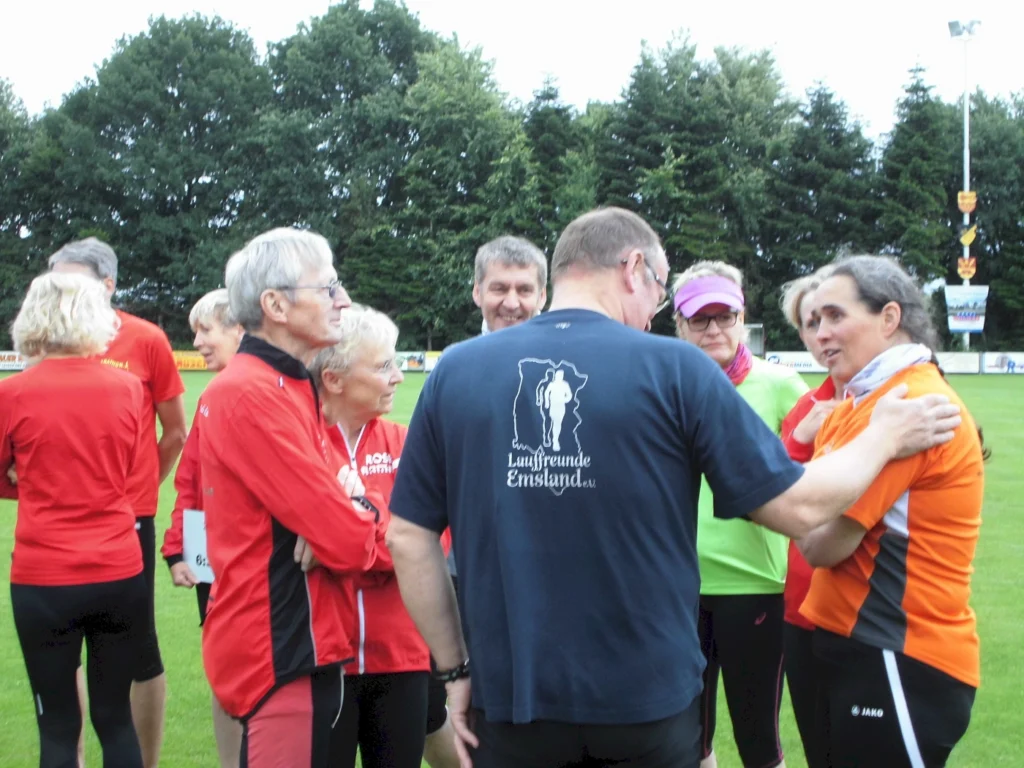 Gruppe von Läufern in bunter Sportkleidung, die sich auf einem Rasenplatz unterhalten, im Hintergrund Bäume.