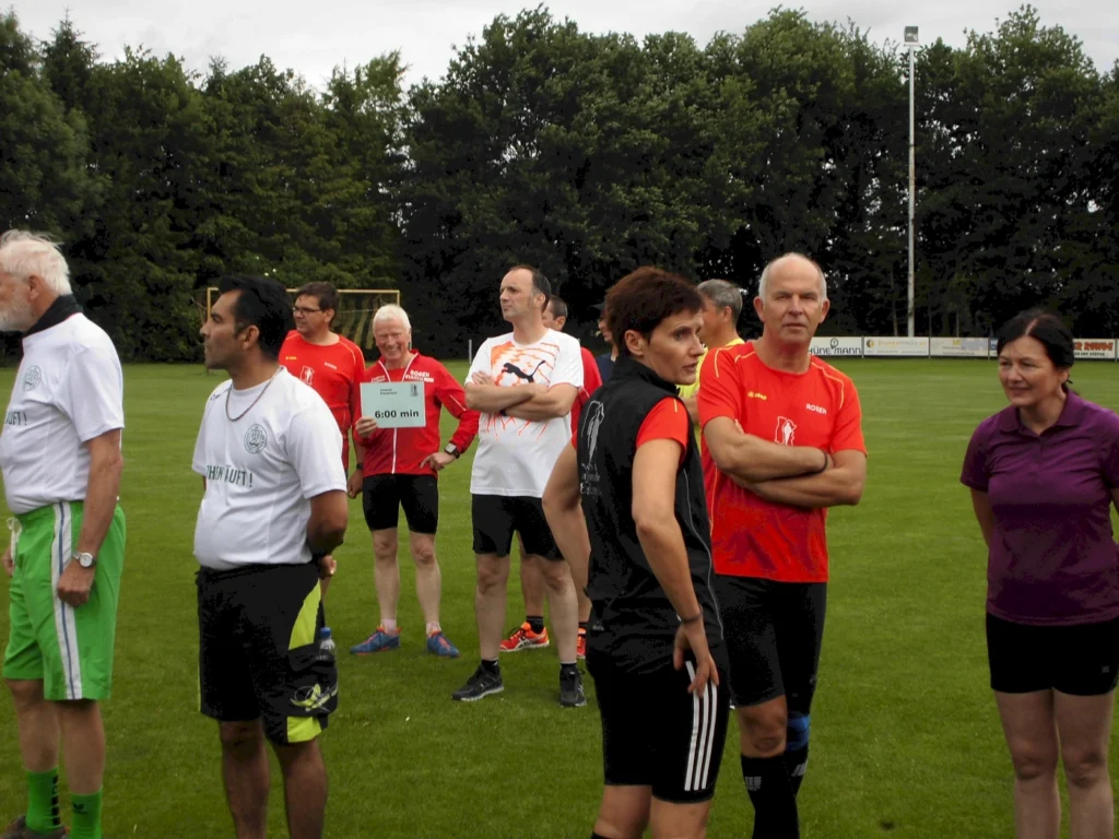 Gruppe von Läufern auf einem Sportfeld versammelt, bereit für einen Lauf. Teilnehmer tragen sportliche Kleidung.