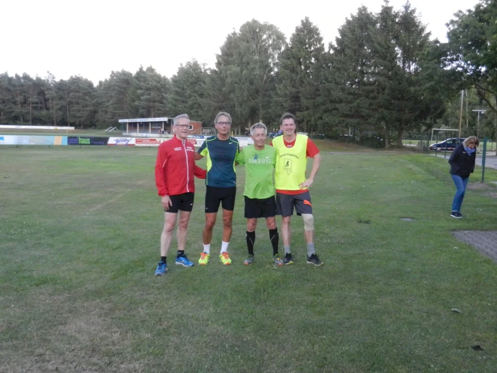 Vier Männer in Sportkleidung stehen auf einem Sportplatz vor Bäumen. Freizeitaktivität und Sport im Freien.