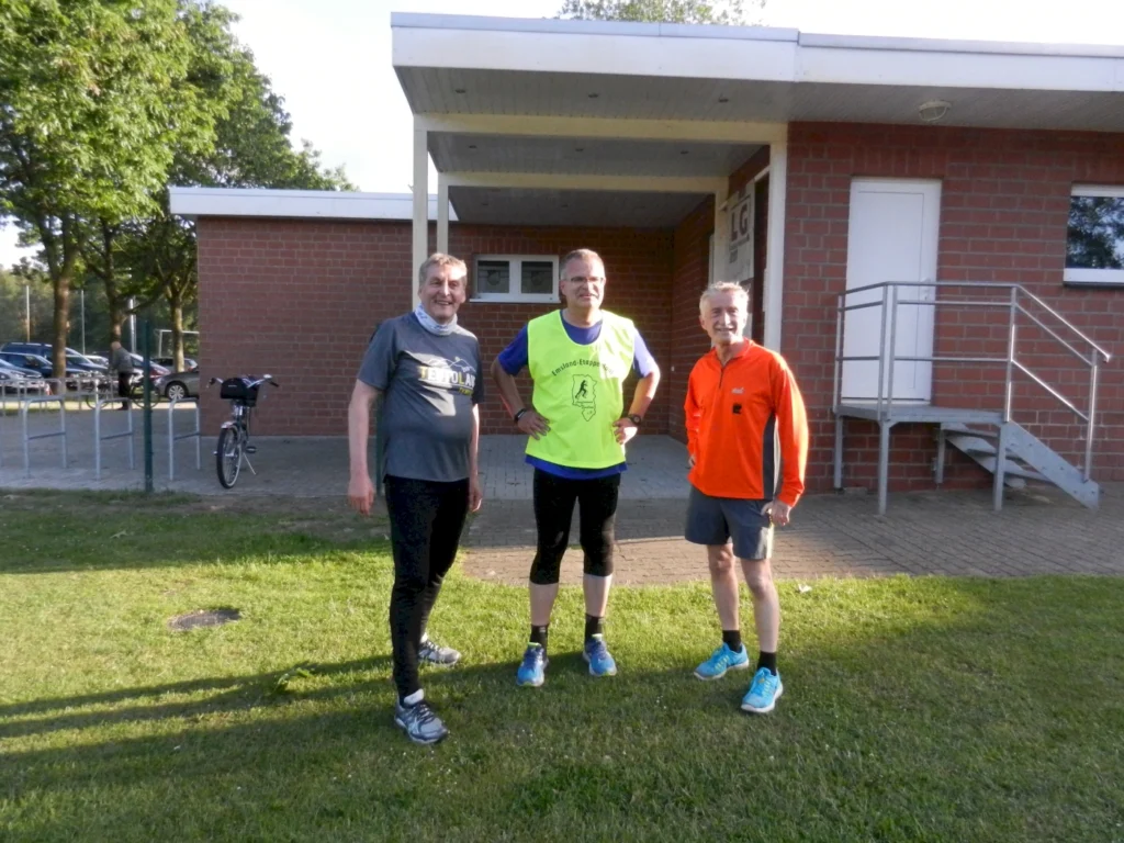 Drei Männer in Sportbekleidung stehen vor einem Gebäude im Freien, bereit für das Joggen.