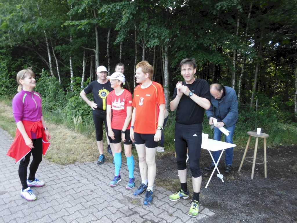 Gruppe von Läufern beim Trainingslauf in Freizeitkleidung im Waldgebiet, ein Mann bereitet Erfrischungen vor.