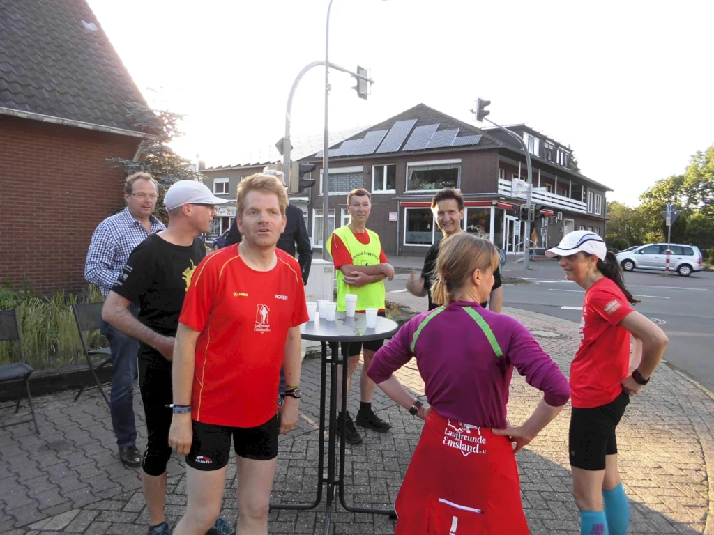 Gruppe von Personen in Sportkleidung, versammelt um einen Tisch im Freien, bei sonnigem Wetter in einer städtischen Umgebung.