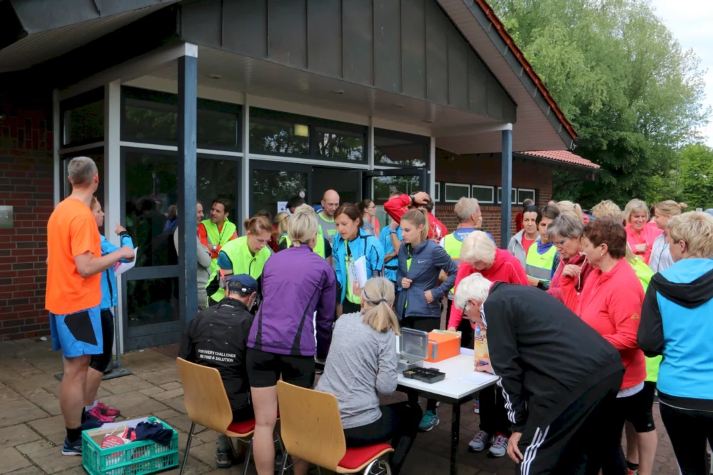 Gruppenevent für Läufer mit Teilnehmern in Sportkleidung, die sich vor einem Gebäude versammeln, um sich anzumelden. Die Szene zeigt eine lebhafte Atmosphäre mit verschiedenen Farben der Laufbekleidung und einer aktiven Diskussion unter den Teilnehmern.
