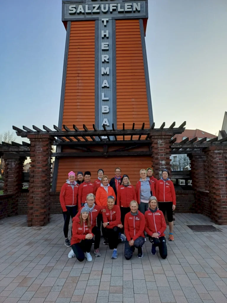 Gruppe von Sportlern in roten Jacken vor dem Salzuflen Thermalbad, umgeben von einer modernen Architektur und einem klaren Himmel.