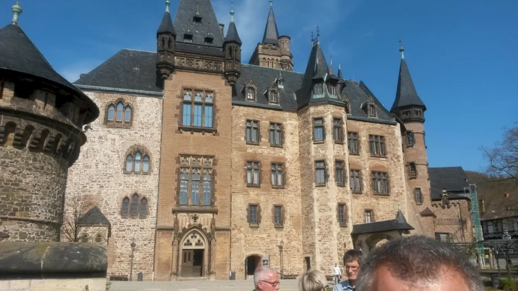 Historisches Schloss mit Türmen und gotischen Fenstern, umgeben von Besuchern und klarem blauen Himmel.