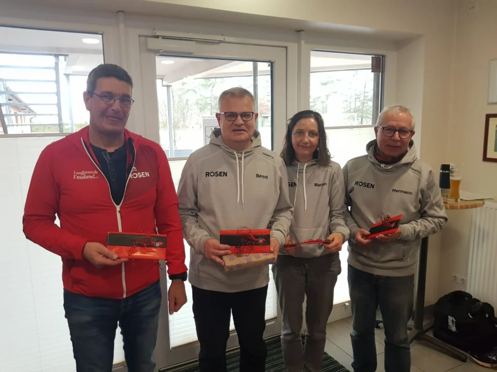 Vier Personen in Sportkleidung mit Geschenken vor geöffneter Glastür, Lauffreunde Emsland Logo auf Jacken.